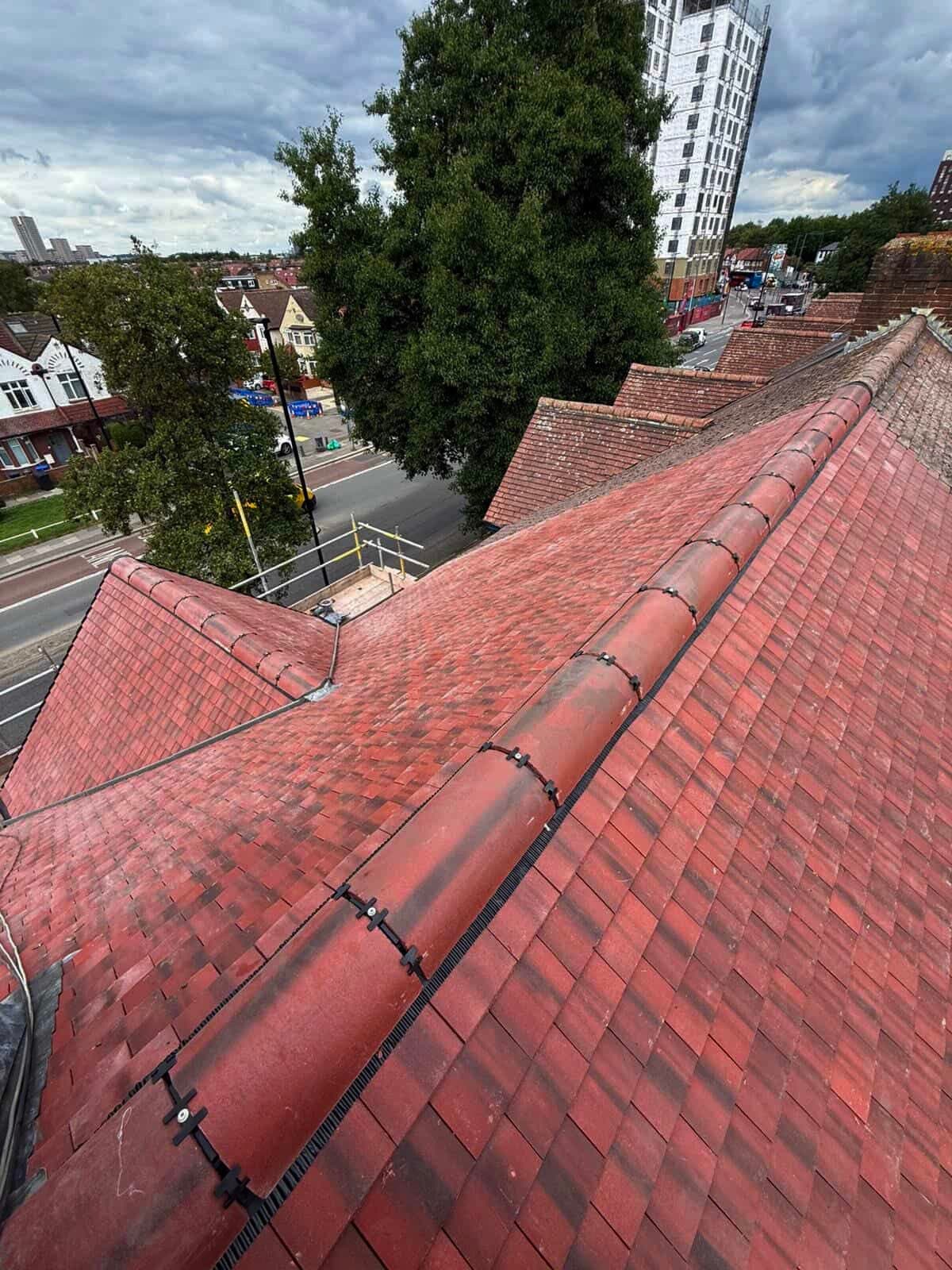 Elevated view of a red tiled roof with ridge tiles secured by black clips.