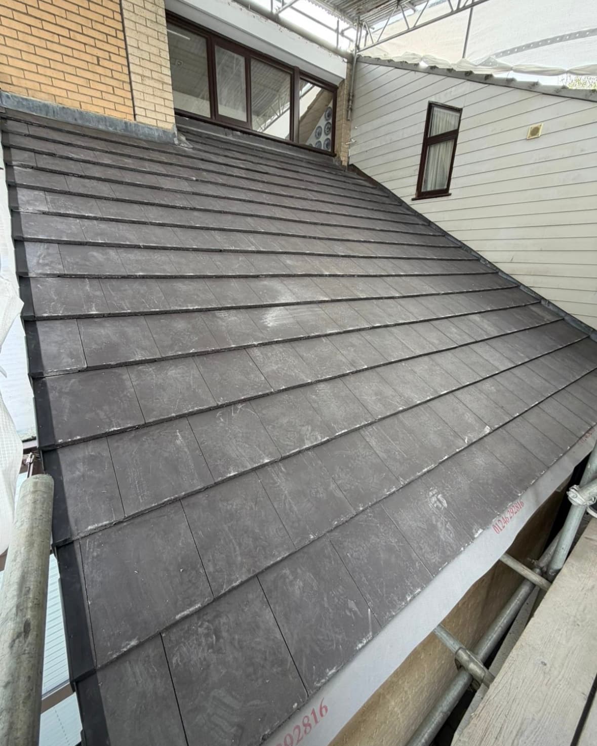 Newly installed dark grey flat tiles on a sloped roof with scaffolding on the side.