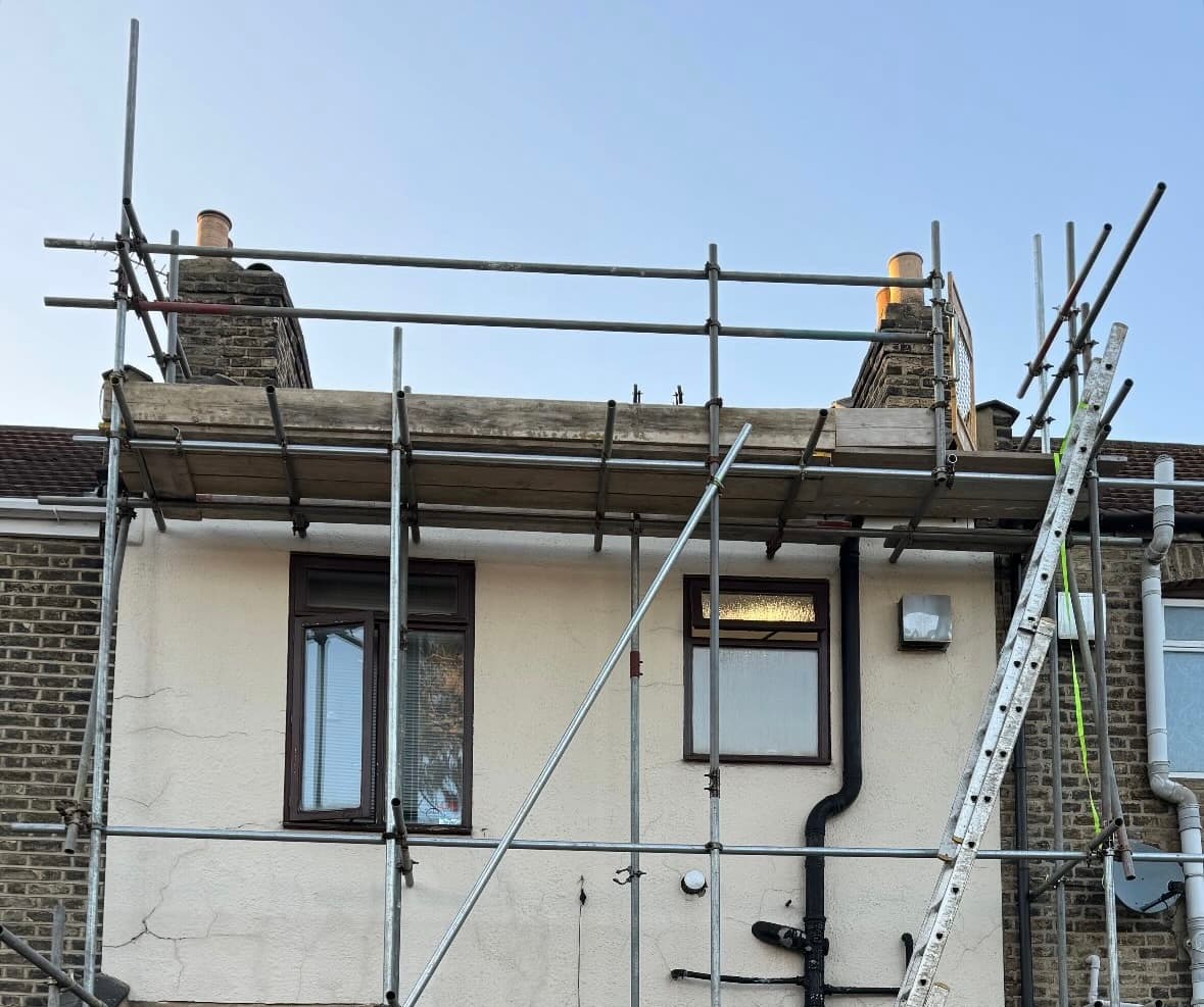 Metal scaffolding with wooden planks and a ladder set against a cream-rendered house for repairs.