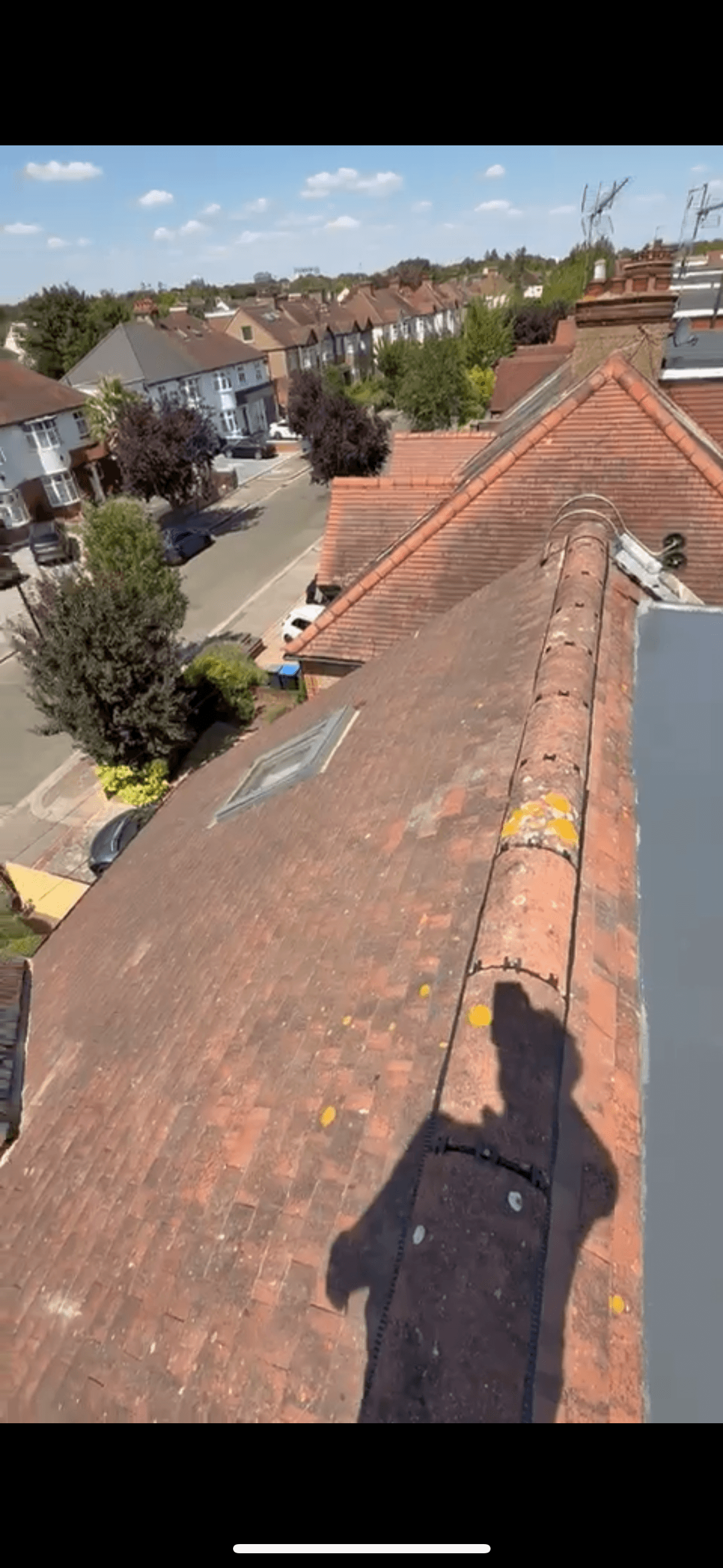 Red-tiled roof with a skylight and person's shadow overlooking a suburban residential street.