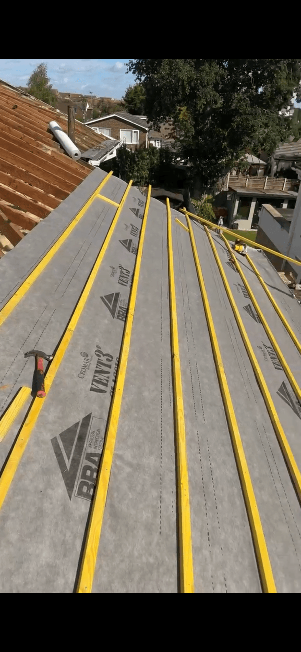Yellow wooden battens installed over grey breathable membrane on a sloped roof under construction.