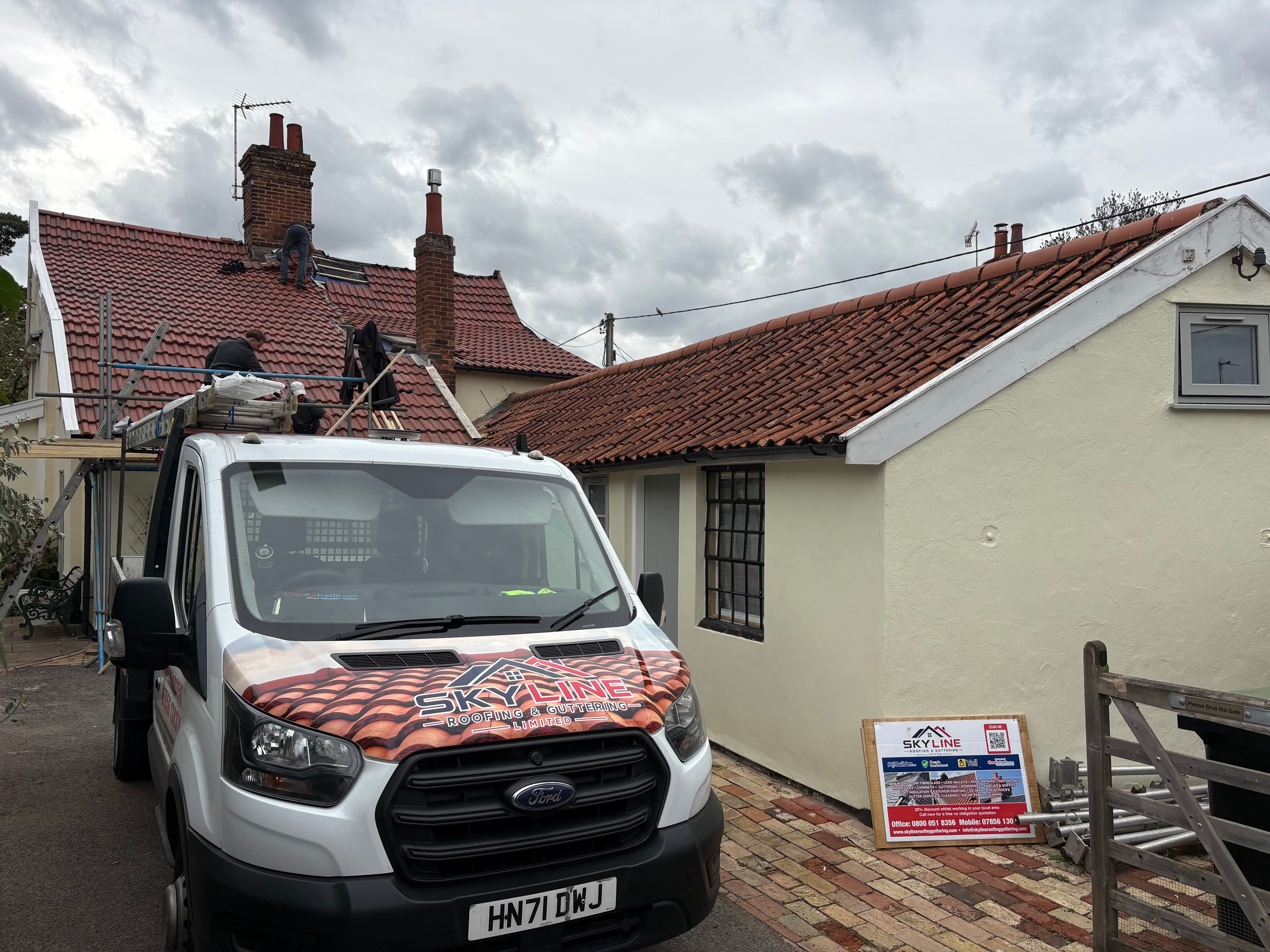 Skyline Roofing van parked outside a house with workers repairing the red tiled roof.